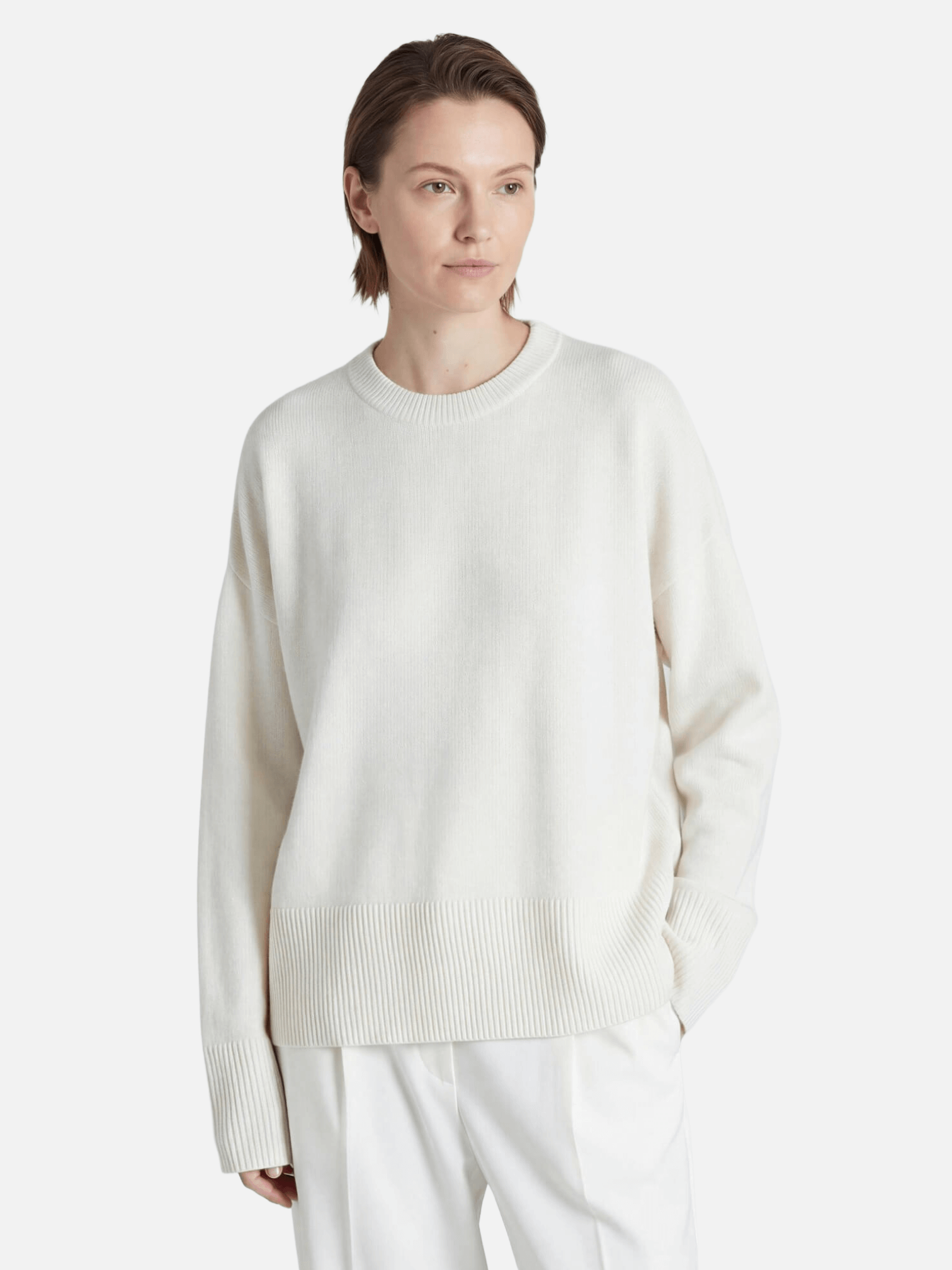 Person wearing a light-colored cashmere sweater and pants on a white background