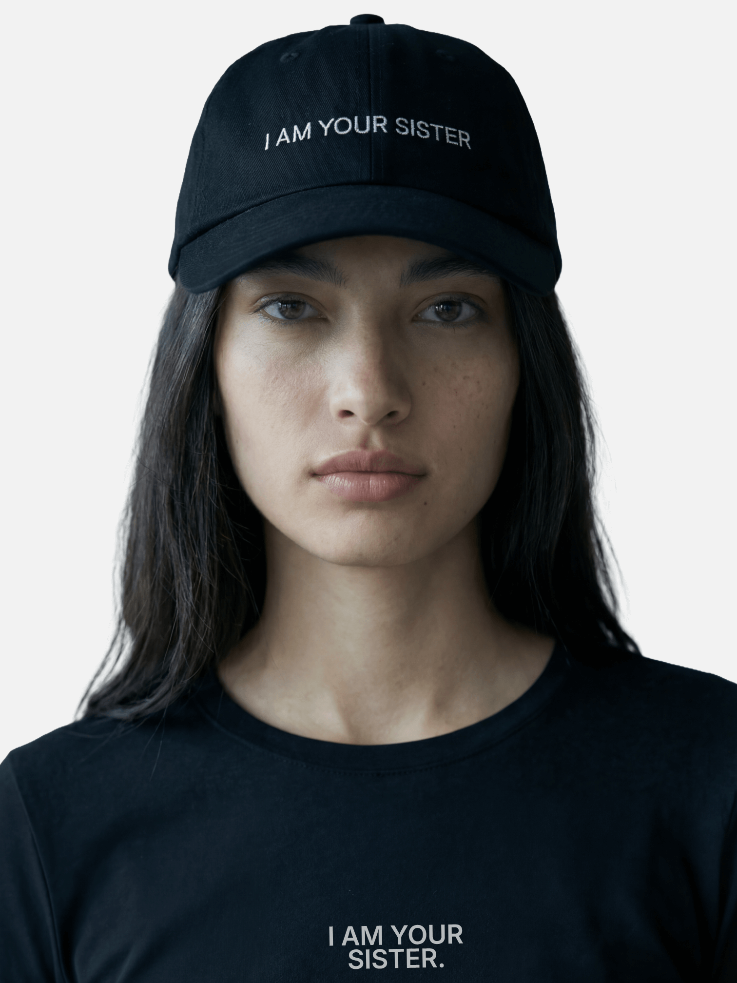 Person wearing a black cap and t-shirt with 'I AM YOUR SISTER' text on a plain background
