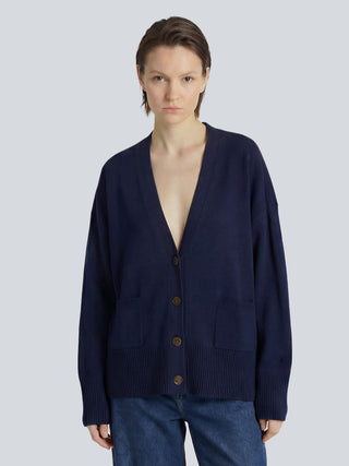 Woman is wearing a navy blue cashmere cardigan on a light gray background