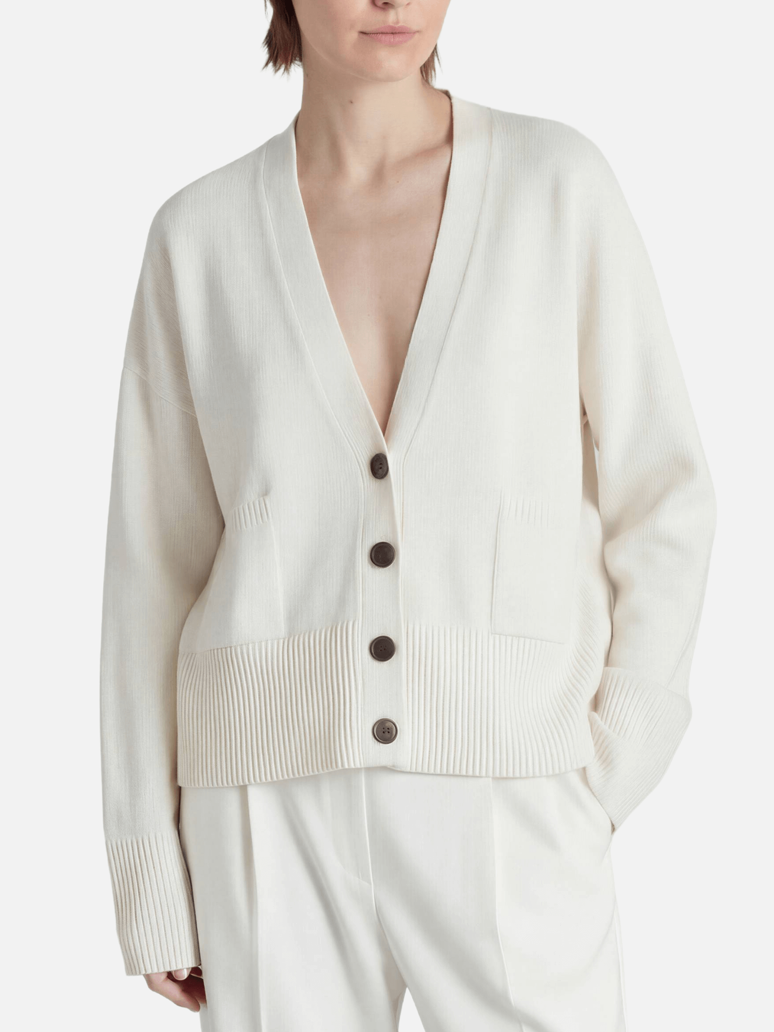 Person wearing a cream-colored cardigan with buttons on a white background